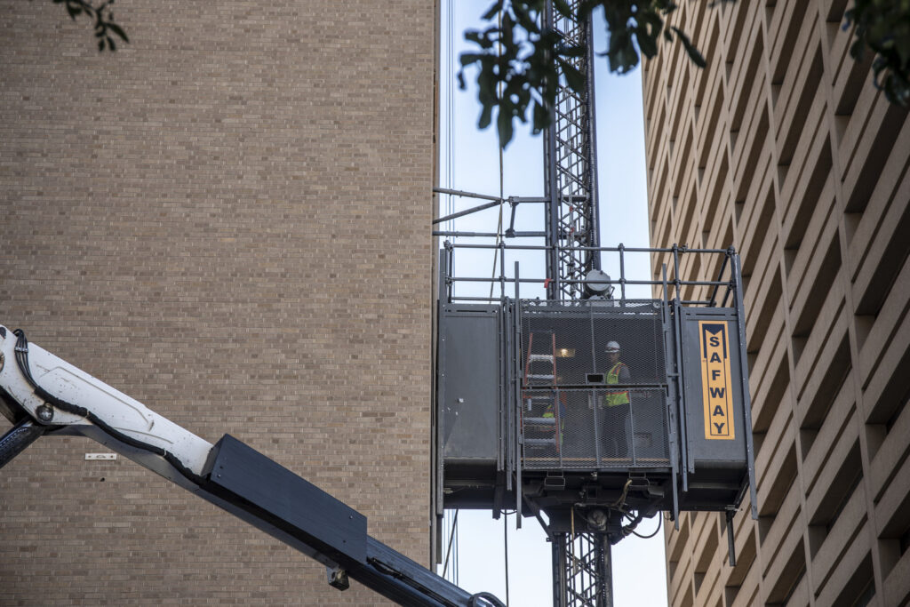 sundt employee-owner riding in construction hoist (external elevator) on side of building.