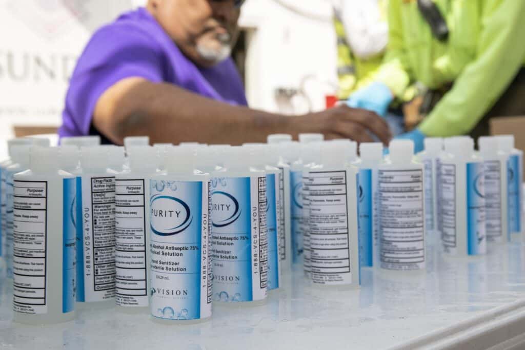 Rick Garcia sits at a table labeling and capping hand sanitizer bottles.