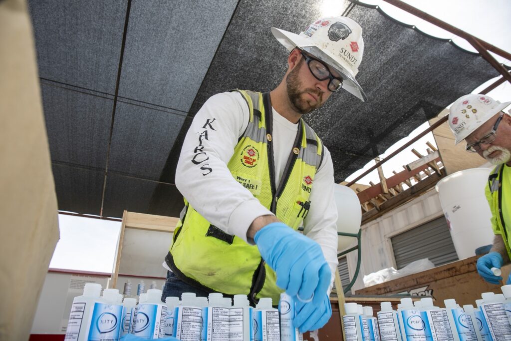 Sundt Employee-Owners Devin Brunzie and Roger Richi label and cap hand sanitizer bottles