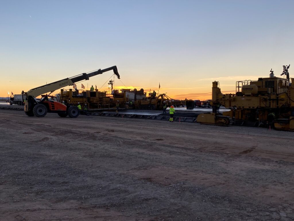 ground silhouette view of two paving machines performing double strikeoff paving at biggs army airfield in El Paso Texas