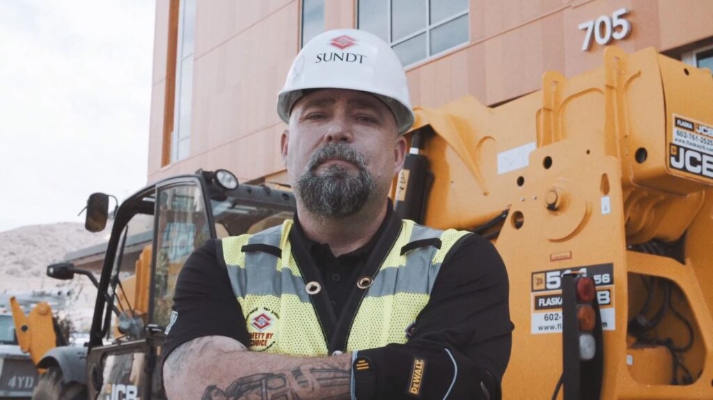 Sundt's Sean Ray stands in front of heavy equipment at a Sundt jobsite
