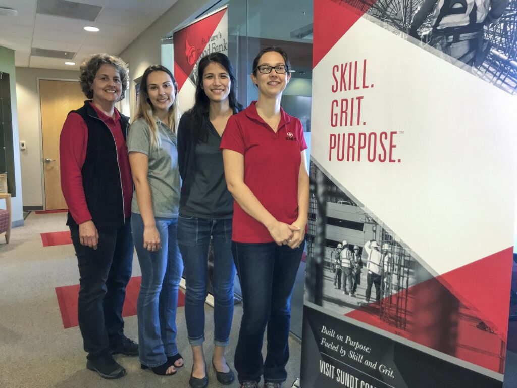 cuatro mujeres que componen el equipo precon de CSU se paran frente al cartel de Sundt que dice Skill, Grit, Purpose