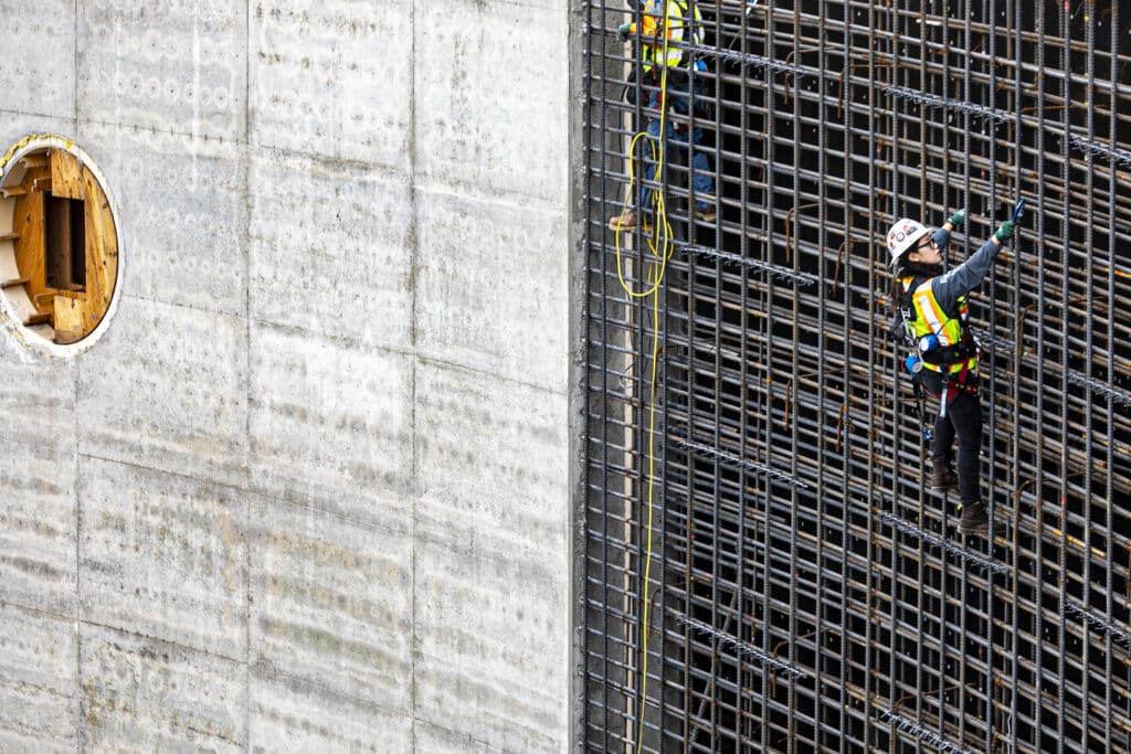 Field Engineer Jackie Odom installs concrete temperature sensors in the walls of underground stormwater containment cistern, harnessed to 35 foot wall