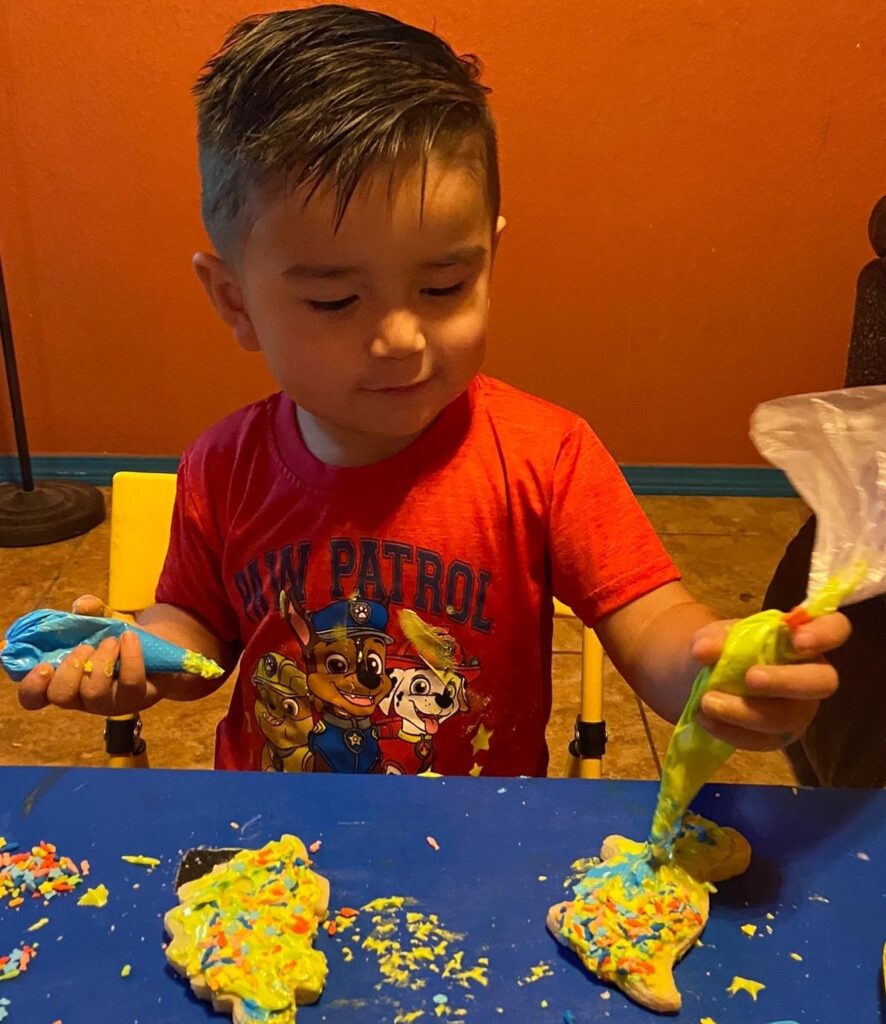 young boy decorates a dinosaur cookie