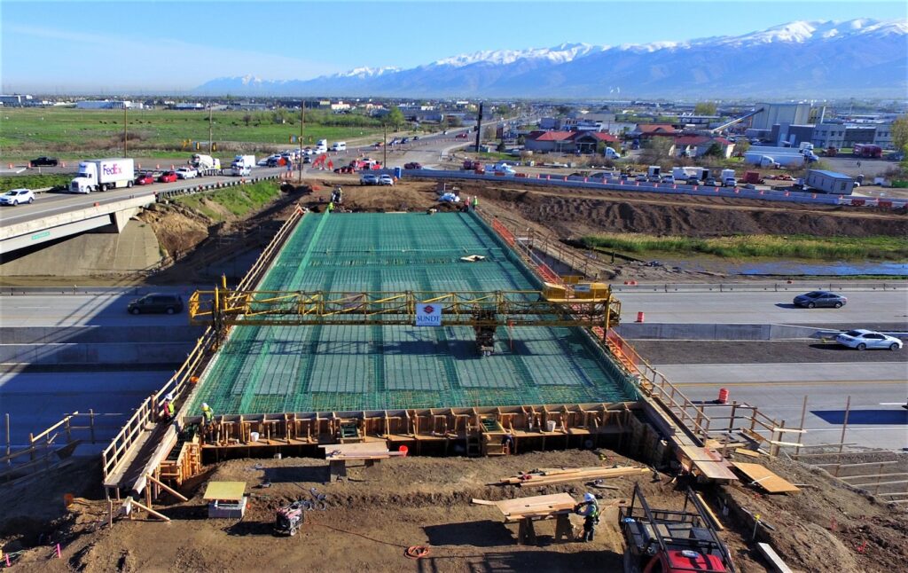 drone aerial shot shows bridge build in progress over interstate with mountains in background