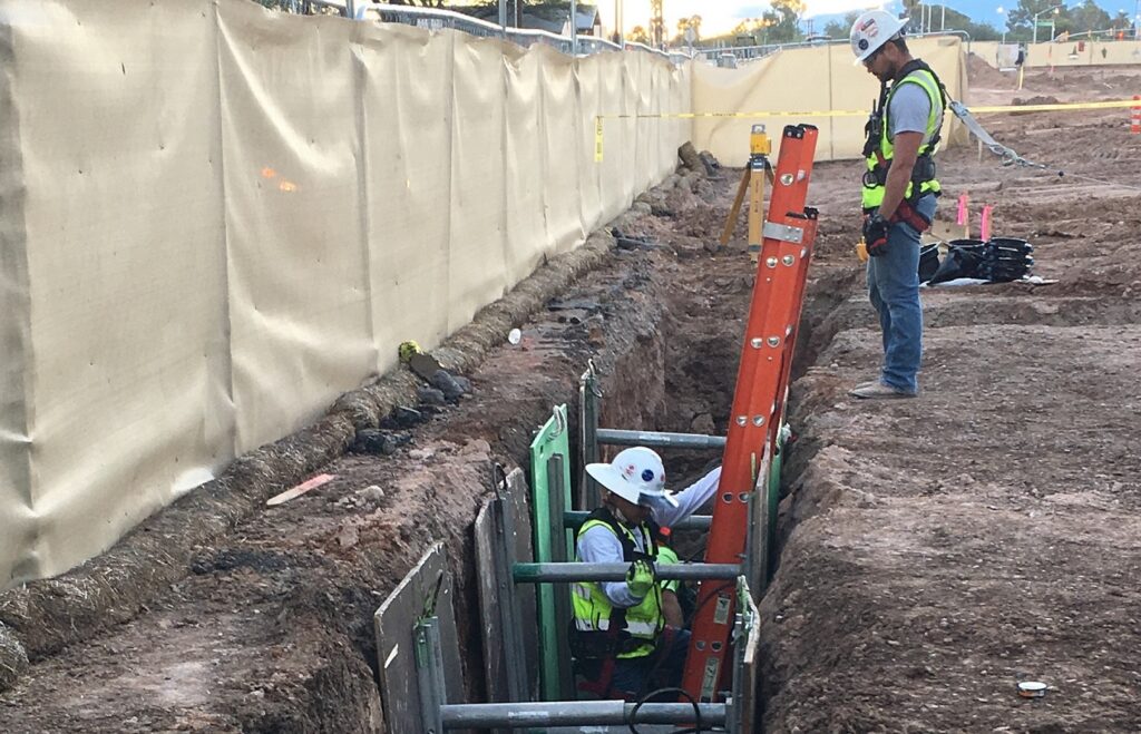 hombre en trinchera y hombre mirando desde arriba para trabajos de instalación de líneas de agua segura