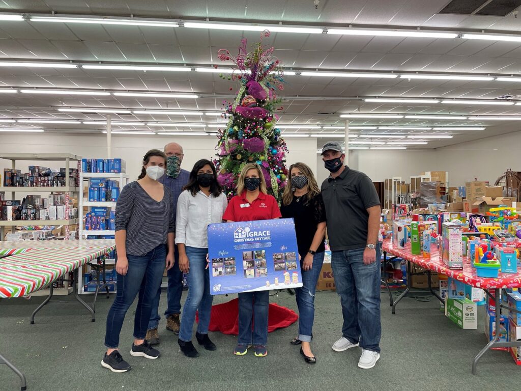 sundt volunteers pose in front of christmas tree and gifts in storefront space that will host christmas cottage event for families