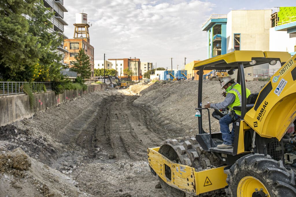 trabajador de la construcción civil compacta el suelo del lecho fluvial con un rodillo de pata de cabra