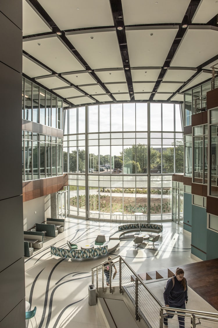 se muestra a dos estudiantes caminando por el atrio de Centennial Hall, con su icónico muro cortina de vidrio curvo de cuatro pisos, rodeado de espacios de laboratorio de alta tecnología