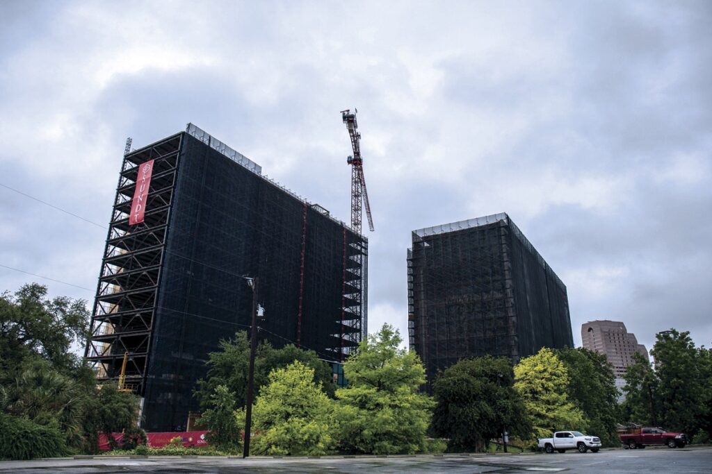 view of two high-rise buildings mid-construction wrapped in black netting containment scaffolding around the building exterior