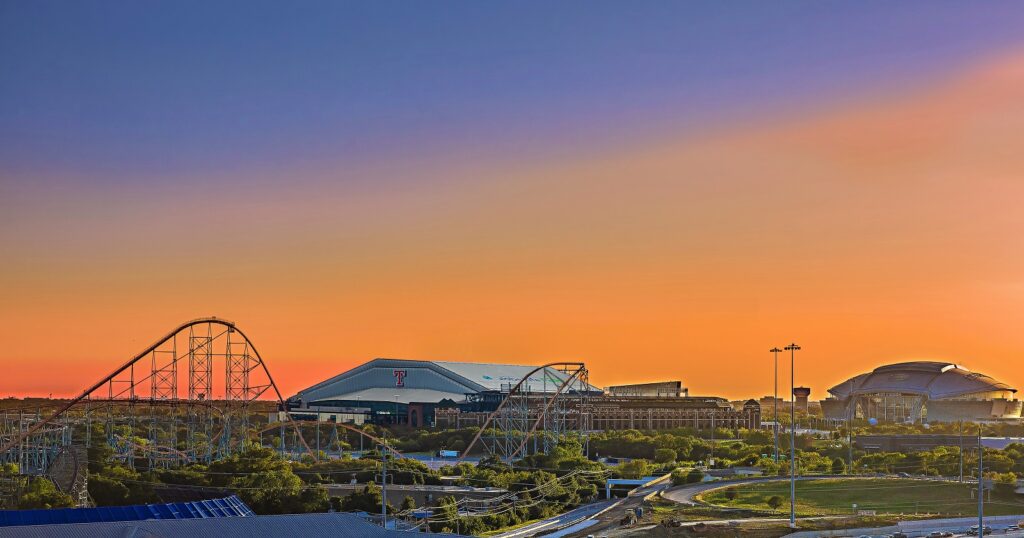 view of sunset over Arlington Texas with six flags roller coasters and Texas Rangers and Dallas Cowboys' AT&T Stadium in background