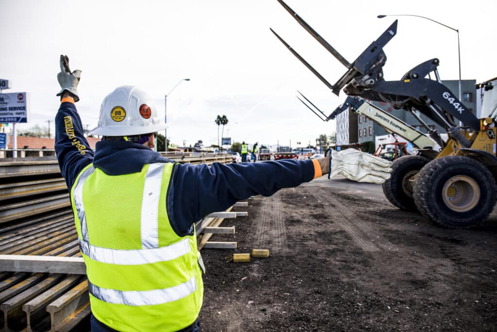 Señalización de abanderados a los operadores de montacargas donde colocar el riel para la construcción del tren ligero