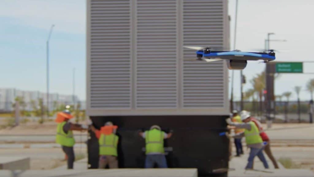 drone flies in foreground of multiple craft workers performing critical pick of large ac unit