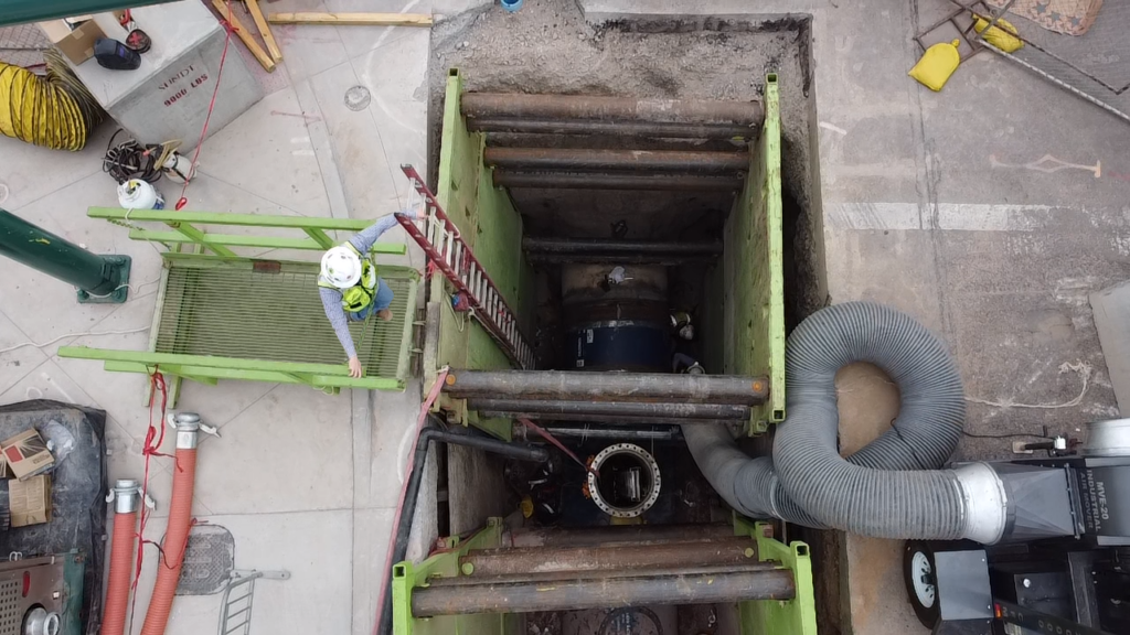 el empleado-propietario de sundt mira hacia abajo a la zanja abierta donde se está instalando la tubería principal de agua de 66 pulgadas
