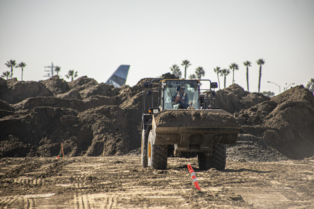 plane takes off behind loader doing earth work at San Diego International Airport