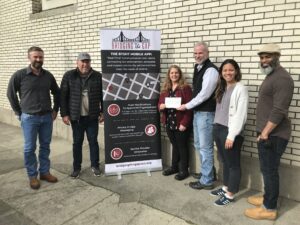 six people posing for a photo outside of a building where two of them are holding a check