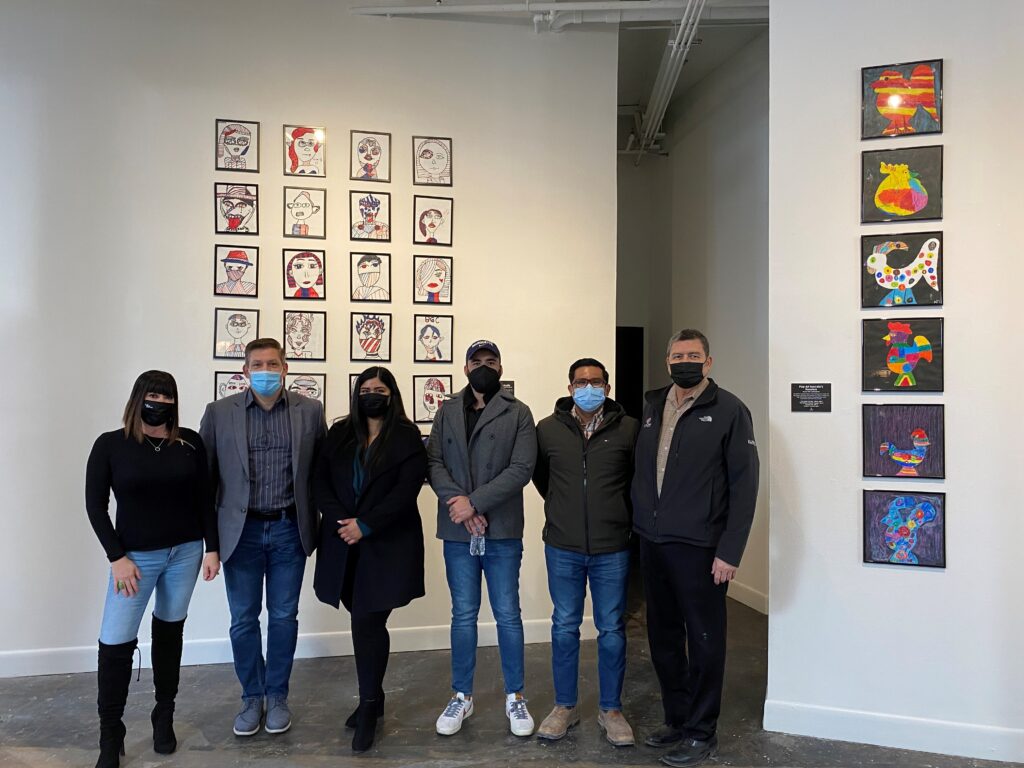 A group of people stand in front of a collage of paintings in an art gallery.