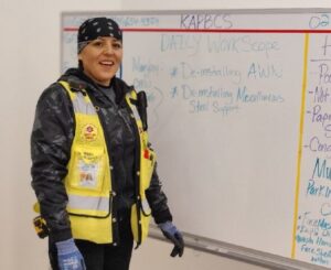 Mujeres con un chaleco amarillo de pie frente a una pizarra sonriendo.