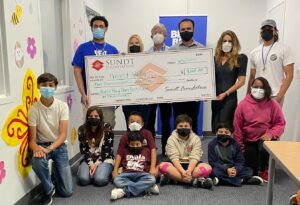 Six people holding a large check with 6 children sitting on the floor below them.