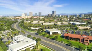 Looking over a street in a business area that has trees and green grass with tall city buildings in the background.