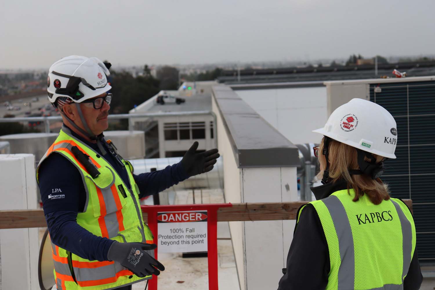 A man and a woman in conversation both wearing bright safety vests and helmets