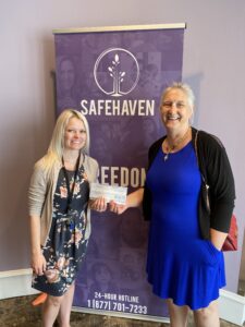 Two women holding a check in front of a sign that reads "SafeHaven".