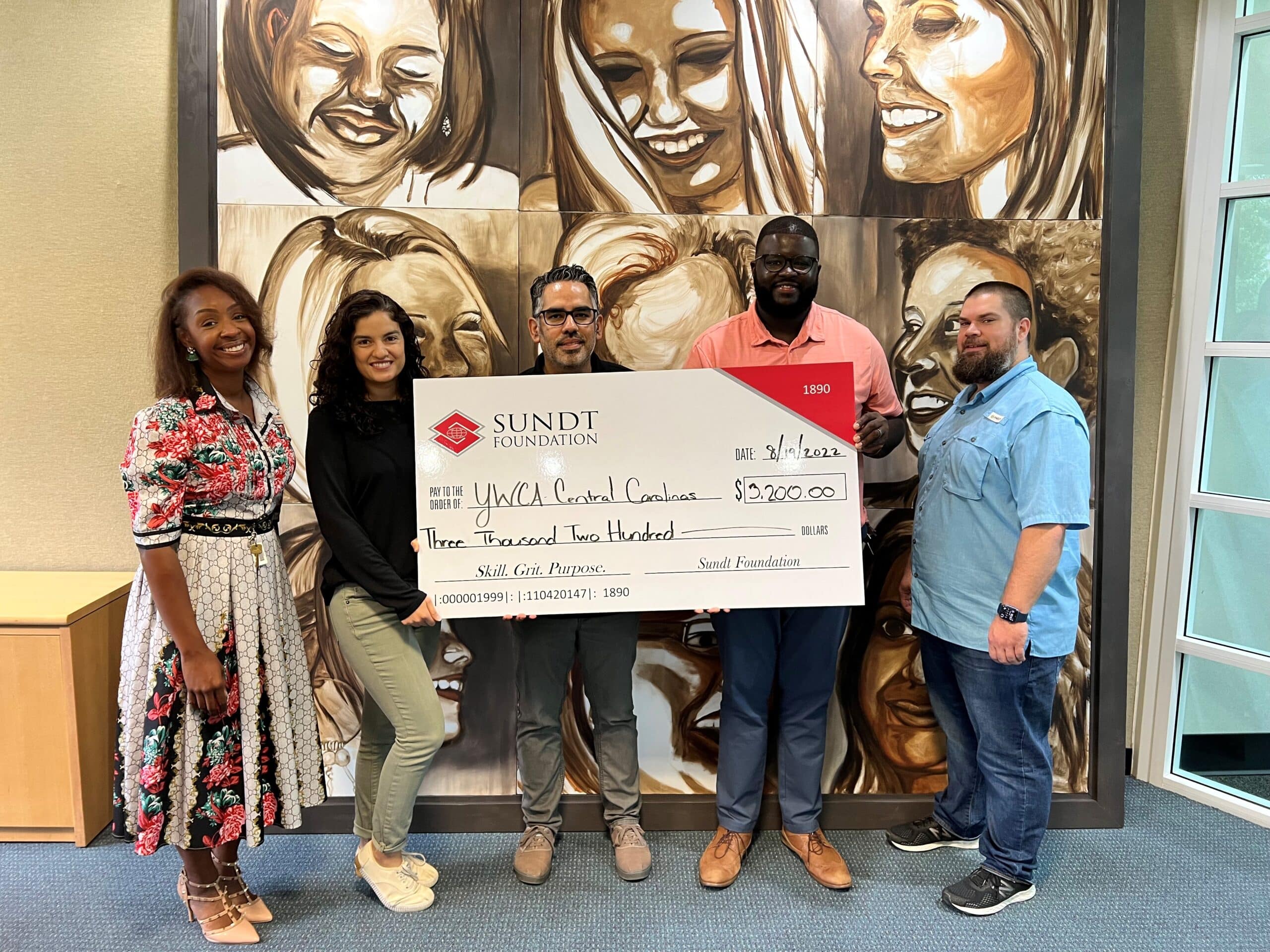 Five people holding a large check standing in front of large art piece. 