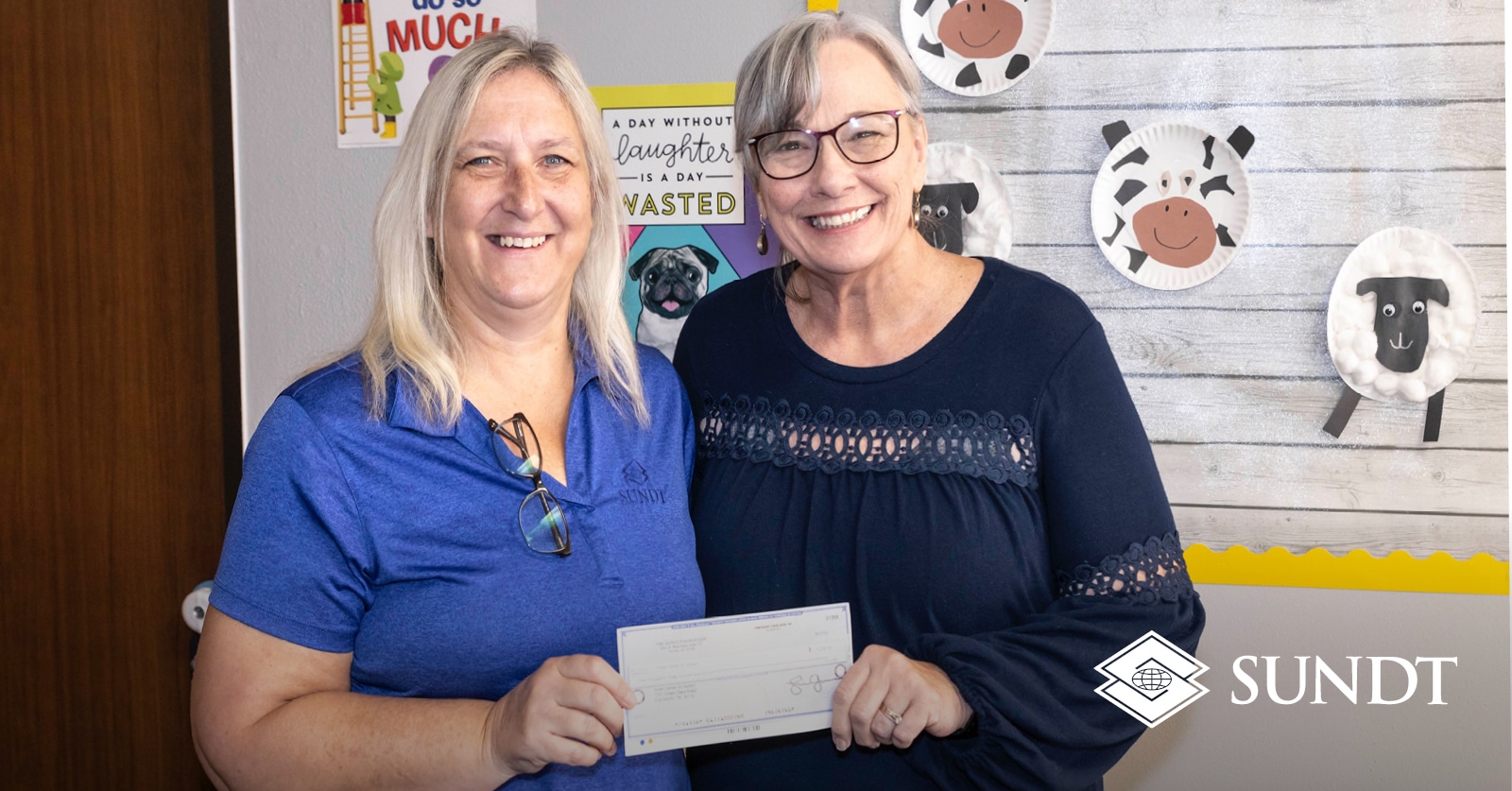 Dos mujeres sosteniendo un cheque frente al arte infantil.