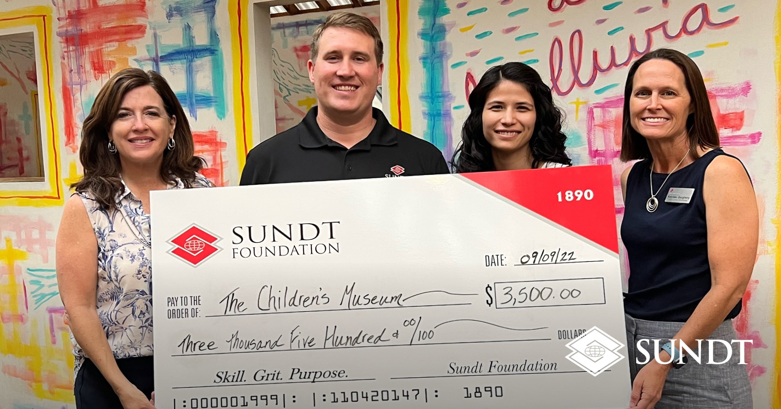 Four people holding large check in front of colorful wall.