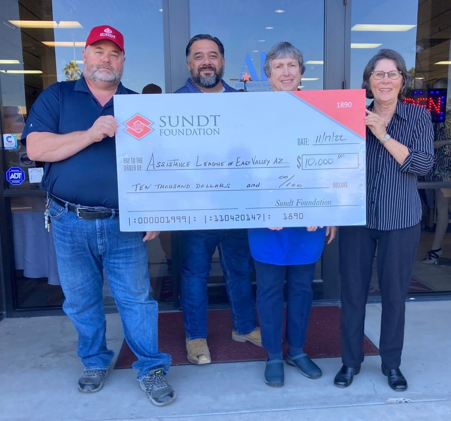 Four people holding large check for $10,000 made out to Assistance League of East Valley by Sundt Foundation