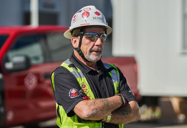 Glen Farlow standing with arms crossed in hard hat and reflective safety vest.