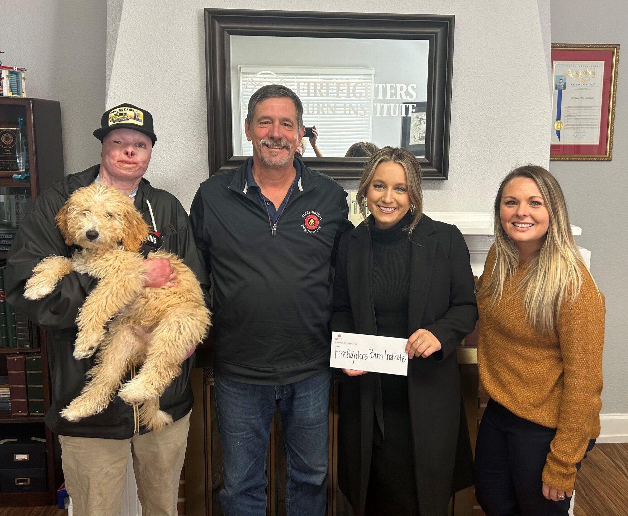 Four people from the Sacramento Firefighters Burn Institute (and one fluffy dog) pose for the camera